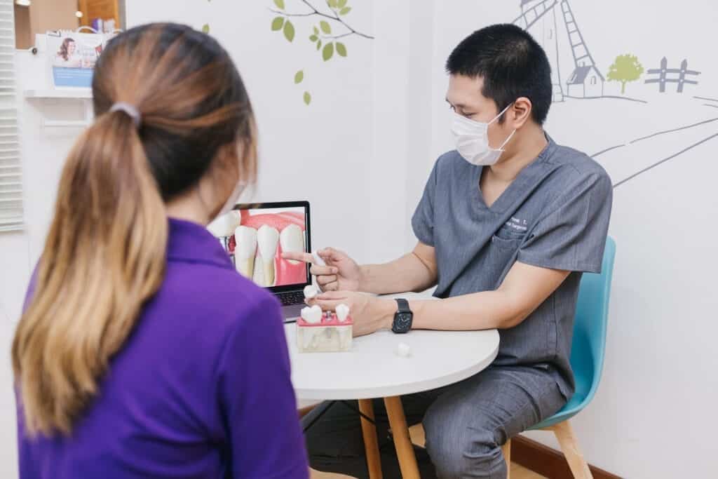 A dentist at Kitcha Dental Clinic explains treatment with a tooth model at a consultation table