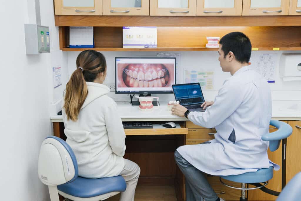 A dentist reviewing smile photos on a laptop and a screen with a patient at Kitcha Dental Clinic