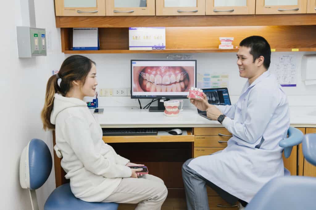 A dentist showing a smile photo on a screen to a patient at the consultation desk at Kitcha Dental Clinic