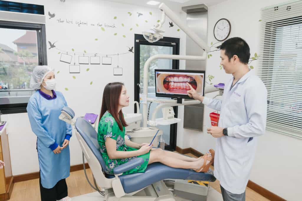A dentist explaining a smile photo on a screen to a patient in the dental chair at Kitcha Dental Clinic