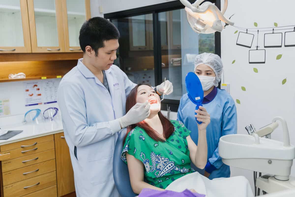Dental professional performing a check-up on a patient at Kitcha Dental Clinic Chiang Mai, with a dental assistant nearby, in a modern dental office setting.