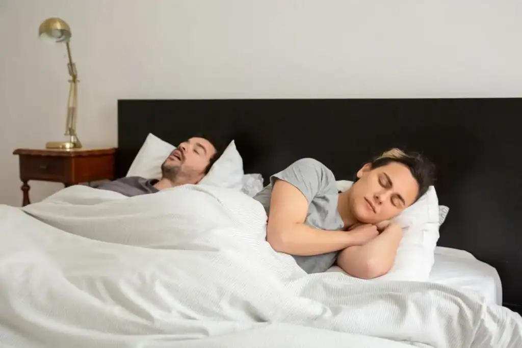 A couple asleep in bed while one partner snores