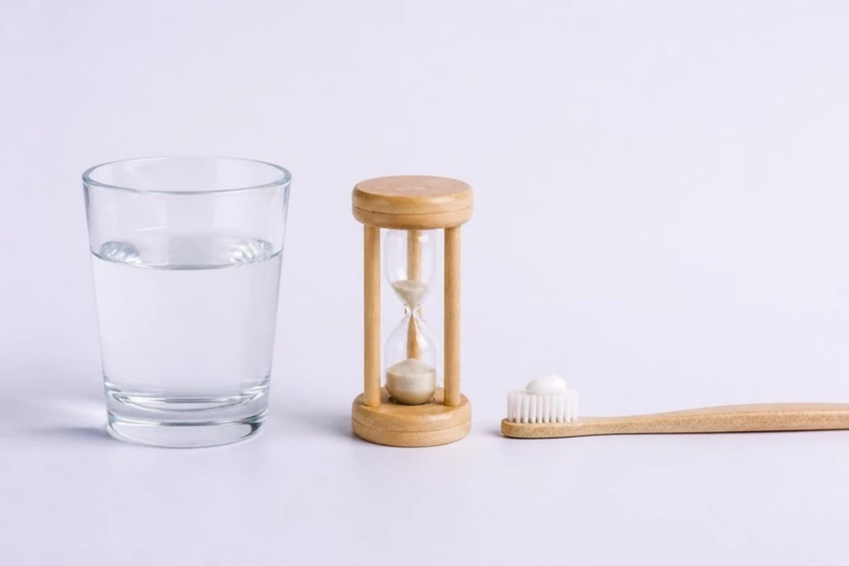 3D插图:一排三样东西——一杯清水、一个小沙漏,以及挤了豌豆大小牙膏的软毛牙刷