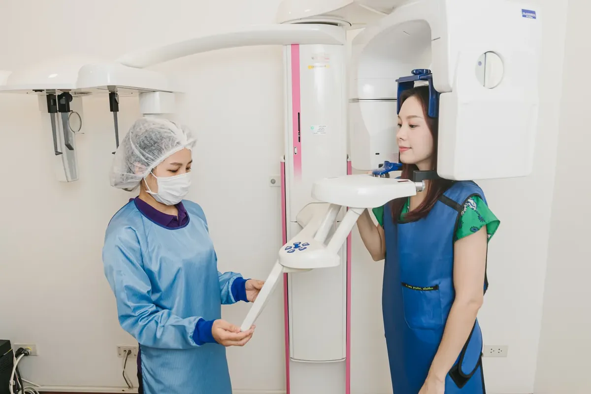 牙科助理为身穿铅防护衣、面带微笑的患者调整 CBCT 三维扫描机的位置