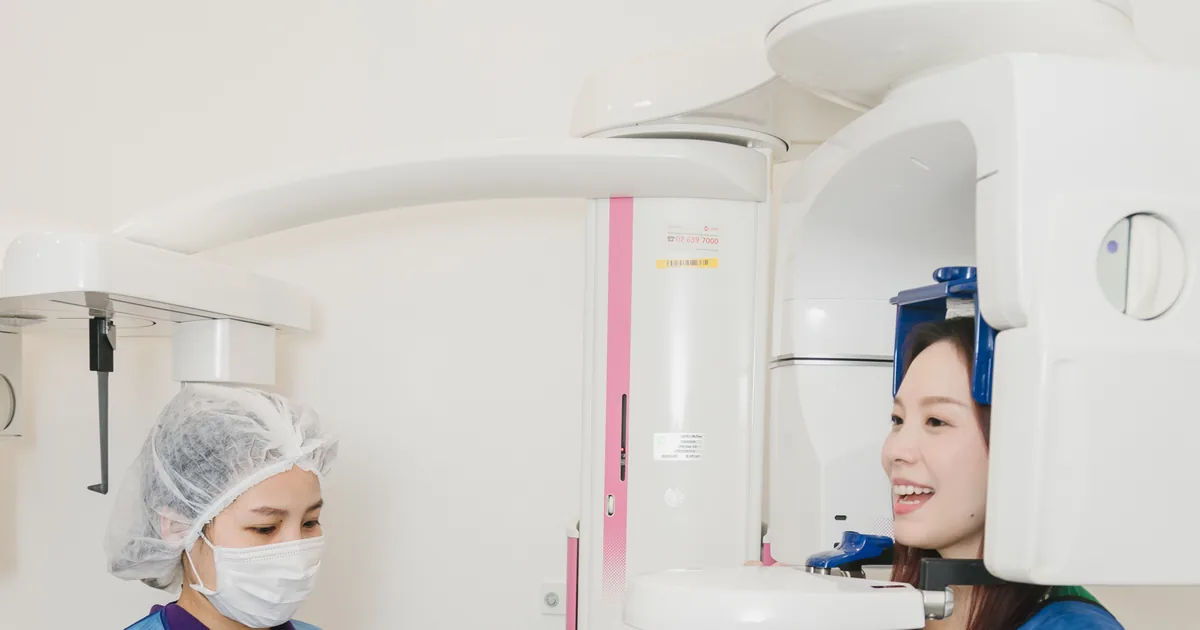 牙科助理为身穿防护围裙、面带微笑的患者在 CBCT 三维扫描仪前调整位置