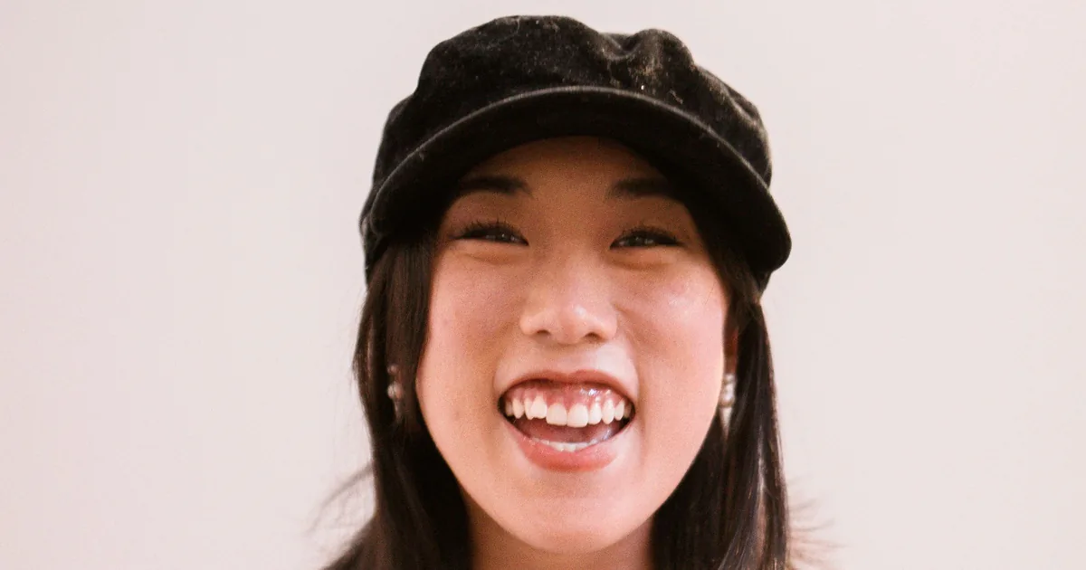一名戴帽子的东亚女士在素色背景前开怀大笑