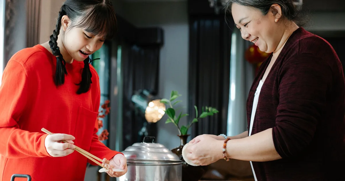 奶奶和孙女在家一起包饺子,面带微笑