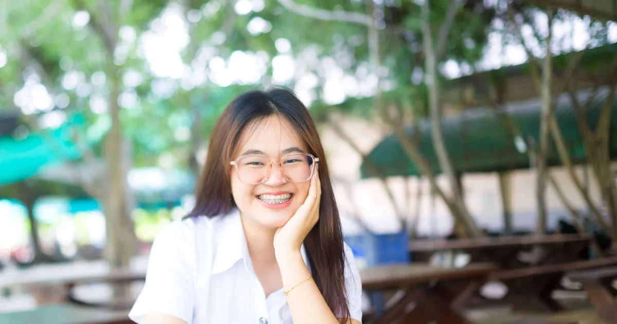 一位戴眼镜和牙套的年轻女士坐在户外桌旁微笑