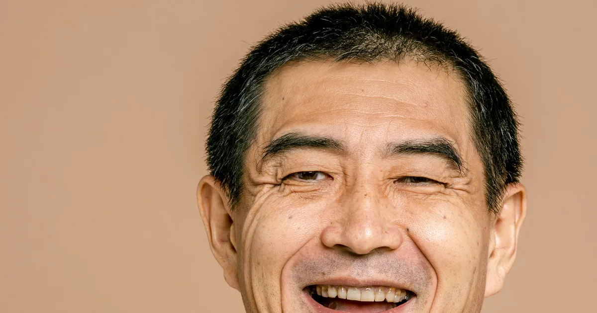 一位开朗的中年亚洲男士在暖色背景前开怀大笑