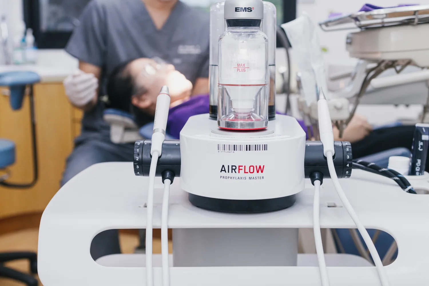 前景为 AIRFLOW 洁牙设备,后方牙医正在为患者清洁牙齿